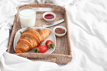 Tray with tasty croissant, strawberry and milk on bed