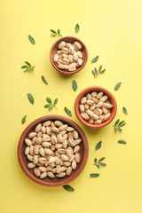 Bowls with tasty pistachio nuts on color background