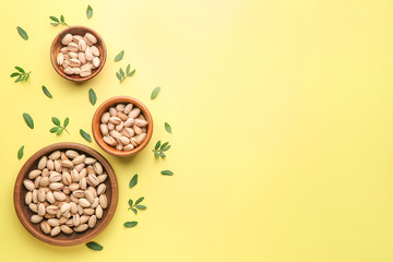 Bowls with tasty pistachio nuts on color background