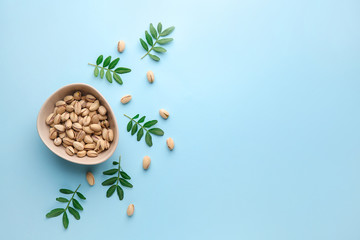Bowl with tasty pistachio nuts on color background