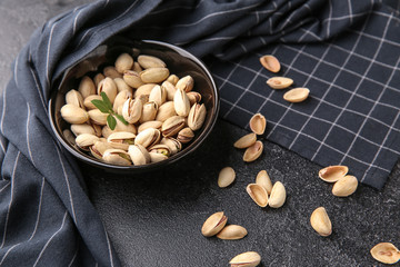 Bowl with tasty pistachio nuts on dark background