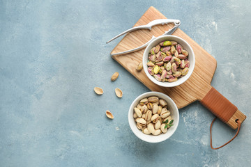 Bowls with tasty pistachio nuts on color background
