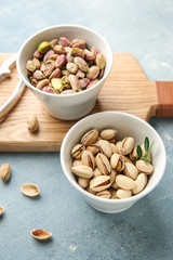Bowls with tasty pistachio nuts on color background