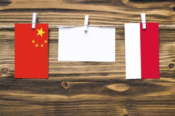 Hanging flags of China and Monaco attached to rope with clothes pins with copy space on white note paper on wooden background.Diplomatic relations between countries.