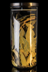 closeup organic dried bay leaves in tall glass jar with metal cap