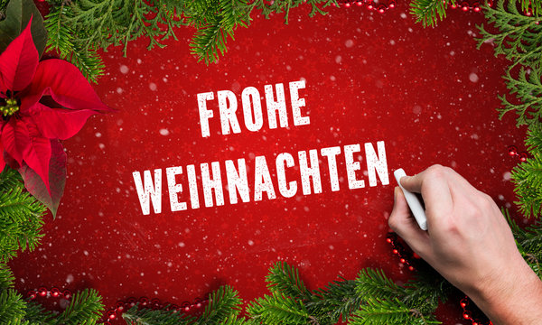 hand writing a Merry Christmas in German message on red background