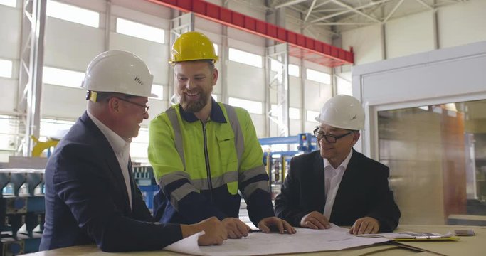 Two engineers in formal suits and technician in uniform on meeting. Colleagues have discussion and analysis of data in technical drafts and blueprints