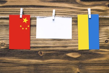 Hanging flags of China and Ukraine attached to rope with clothes pins with copy space on white note paper on wooden background.Diplomatic relations between countries.