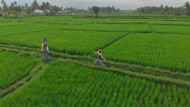 Aerial shot of a woman practicing yoga on a marvelous rice field during sunrise-sunset