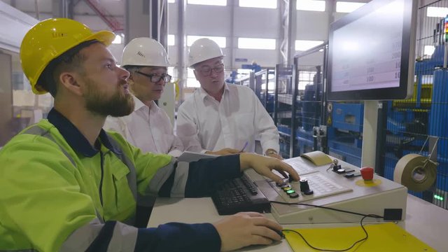 Inside the heavy industry factory shot of industrial engineers and worker working with cnc machine. White collars asian and caucasian talk and discuss data from display