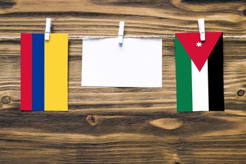 Hanging flags of Colombia and Jordan attached to rope with clothes pins with copy space on white note paper on wooden background.Diplomatic relations between countries.