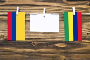 Hanging flags of Colombia and Mauritius attached to rope with clothes pins with copy space on white note paper on wooden background.Diplomatic relations between countries.