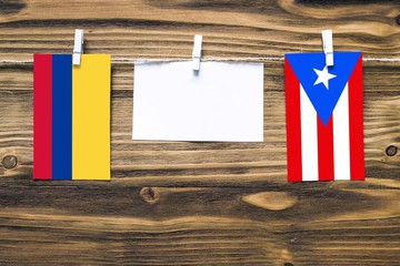 Hanging flags of Colombia and Puerto Rico attached to rope with clothes pins with copy space on white note paper on wooden background.Diplomatic relations between countries.