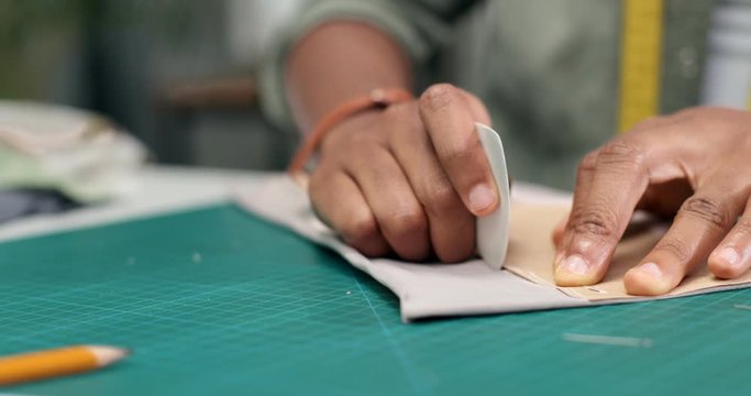 Close up of the hands of the African American woman who is clothing designer doing outlines for the new collection on the table in studio.