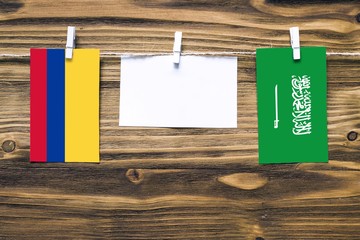Hanging flags of Colombia and Saudi Arabia attached to rope with clothes pins with copy space on white note paper on wooden background.Diplomatic relations between countries.