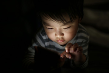 暗い中でスマートフォンを使う男の子