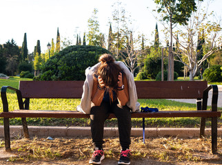 woman dressed in sportswear sitting on a park bench with her head bowed