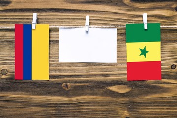 Hanging flags of Colombia and Senegal attached to rope with clothes pins with copy space on white note paper on wooden background.Diplomatic relations between countries.