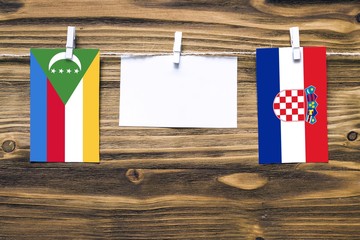 Hanging flags of Comoros and Croatia attached to rope with clothes pins with copy space on white note paper on wooden background.Diplomatic relations between countries.