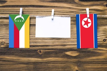 Hanging flags of Comoros and North Korea attached to rope with clothes pins with copy space on...