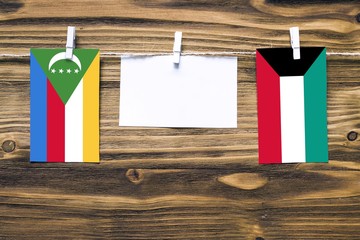Hanging flags of Comoros and Kuwait attached to rope with clothes pins with copy space on white...