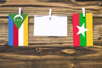 Hanging flags of Comoros and Myanmar attached to rope with clothes pins with copy space on white...