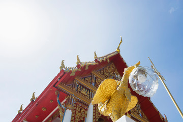 a low angle view of a golden bird statue with a red and gold building behind it, against a bright blue sky.