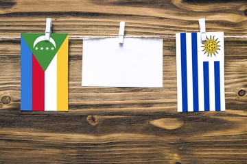 Hanging flags of Comoros and Uruguay attached to rope with clothes pins with copy space on white...