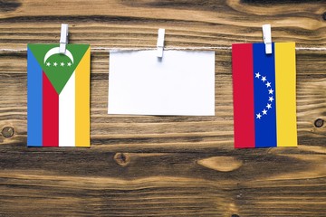 Hanging flags of Comoros and Venezuela attached to rope with clothes pins with copy space on white...