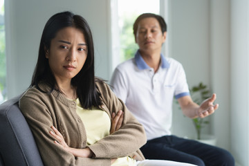 Asian couple having relation problem. Wife crying and sitting separate with her husband at home after quarrel.