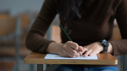 Young female university student concentrate doing  examination in classroom. Girl student writes the exercise of the examinations. University classroom. Classroom chairs. University student.