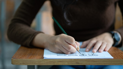 Young female university student concentrate doing  examination in classroom. Girl student writes the exercise of the examinations. University classroom. Classroom chairs. University student.
