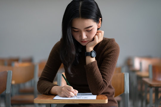 Young female university student concentrate doing  examination in classroom. Girl student writes the exercise of the examinations. University classroom. Classroom chairs. University student.