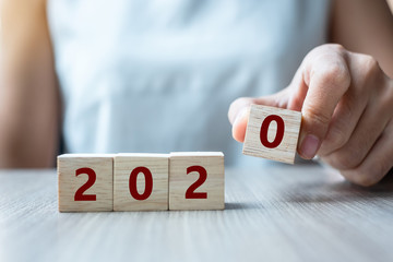 Business woman hand holding wooden cube with 2020 word on table background. Resolution, strategy,...