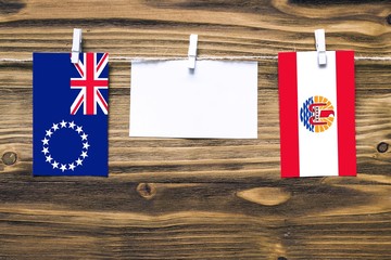 Hanging flags of Cook Islands and French Polynesia attached to rope with clothes pins with copy space on white note paper on wooden background.Diplomatic relations between countries.