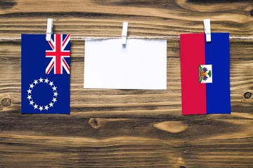 Hanging flags of Cook Islands and Haiti attached to rope with clothes pins with copy space on white...