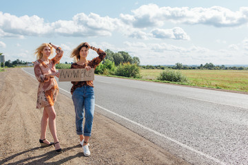 Two beautiful girls hitchhiking and vote with a sign ANYWHERE on road. Copy space.