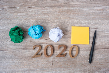 2020 Happy New year with yellow note, crumbled paper and pen on wooden table background. New You, Start, Idea, Creative, Innovation, Resolution and Goal concept