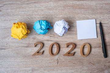 2020 NEW YEAR WITH blank yellow note  and crumbled paper on wooden table background. NEW START, Strategy and Goal concept