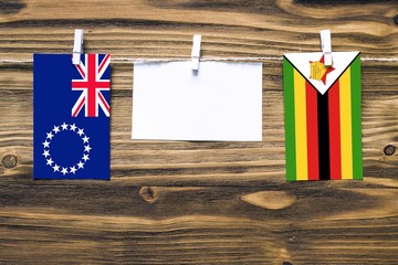 Hanging flags of Cook Islands and Zimbabwe attached to rope with clothes pins with copy space on white note paper on wooden background.Diplomatic relations between countries.