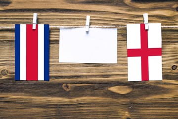 Hanging flags of Costa Rica and England attached to rope with clothes pins with copy space on white note paper on wooden background.Diplomatic relations between countries.