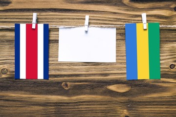 Hanging flags of Costa Rica and Gabon attached to rope with clothes pins with copy space on white...