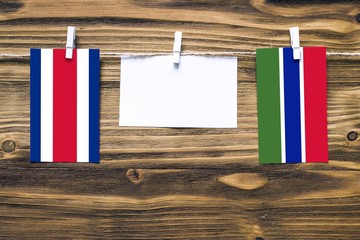 Hanging flags of Costa Rica and Gambia attached to rope with clothes pins with copy space on white note paper on wooden background.Diplomatic relations between countries.