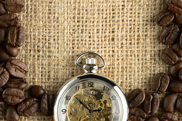 coffee background of roasted coffee beans and pocket watch on gunny cloth background in concept of coffee time