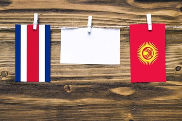Hanging flags of Costa Rica and Kyrgyzstan attached to rope with clothes pins with copy space on white note paper on wooden background.Diplomatic relations between countries.