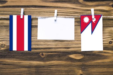 Hanging flags of Costa Rica and Nepal attached to rope with clothes pins with copy space on white note paper on wooden background.Diplomatic relations between countries.