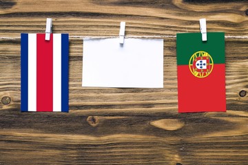 Hanging flags of Costa Rica and Portugal attached to rope with clothes pins with copy space on white note paper on wooden background.Diplomatic relations between countries.