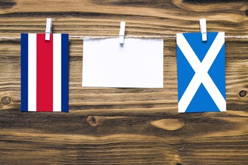 Hanging flags of Costa Rica and Scotland attached to rope with clothes pins with copy space on white note paper on wooden background.Diplomatic relations between countries.