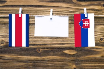 Hanging flags of Costa Rica and Slovakia attached to rope with clothes pins with copy space on white note paper on wooden background.Diplomatic relations between countries.