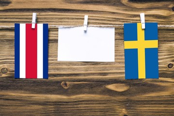 Hanging flags of Costa Rica and Sweden attached to rope with clothes pins with copy space on white note paper on wooden background.Diplomatic relations between countries.